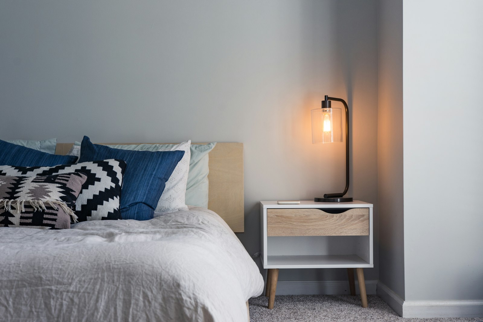 A tidy motel room with a made bed and a bedside lamp (placeholder photo)